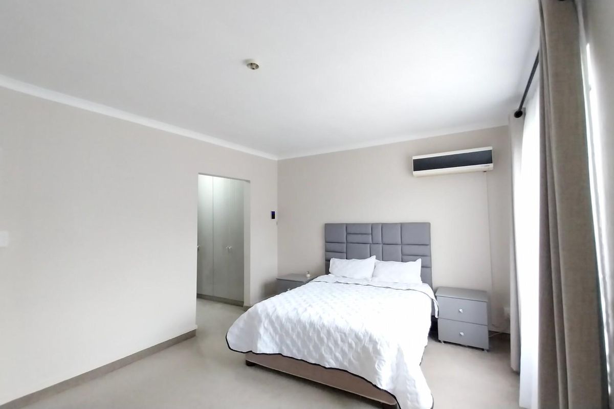 A well-maintained bedroom featuring neutral wall tones, built-in cupboards, and a wall-mounted air conditioning unit.