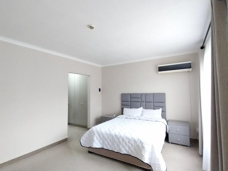 A well-maintained bedroom featuring neutral wall tones, built-in cupboards, and a wall-mounted air conditioning unit.