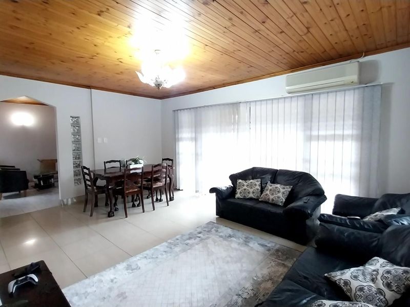 Spacious open-plan living and dining area featuring a timber-clad ceiling, tiled flooring, and a glass block feature wall with integrated air conditioning.
