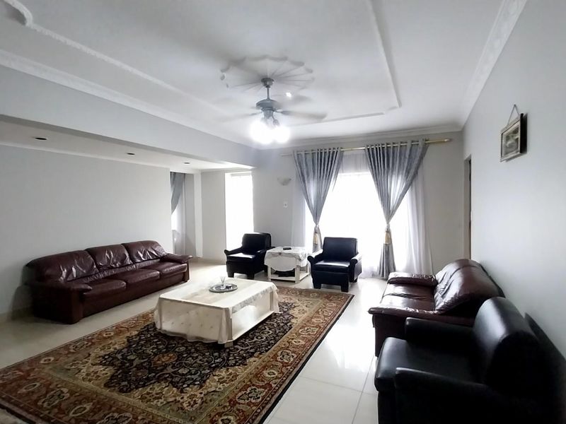 Spacious living room featuring tiled flooring, decorative ceiling roses, and recessed lighting, offering a bright and comfortable area for relaxation.