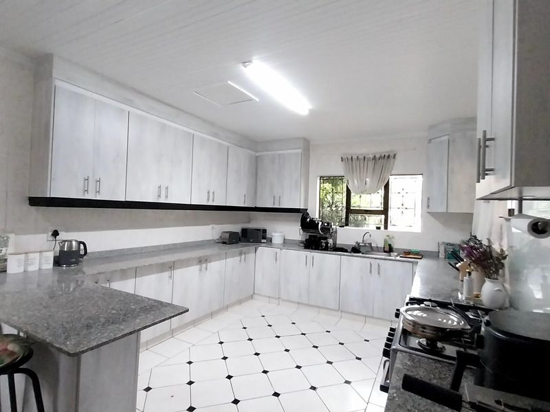 Spacious kitchen featuring extensive built-in cabinetry, granite countertops, a breakfast bar, and a gas hob, finished with classic tiled flooring.