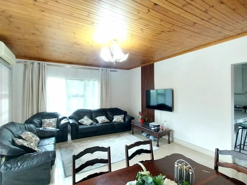Open plan living and dining area featuring a timber ceiling, tiled floors, and wall-mounted air conditioning, with an adjacent kitchen visible.