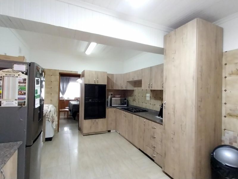 Functional kitchen featuring light wood-look cabinetry, built-in oven, gas hob, and tiled splashbacks with neutral floor tiles.