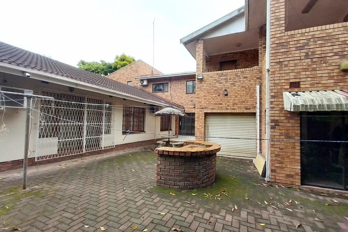 Rear courtyard area featuring brick paving, a built-in brick braai, and access to the garage and main dwelling structure.