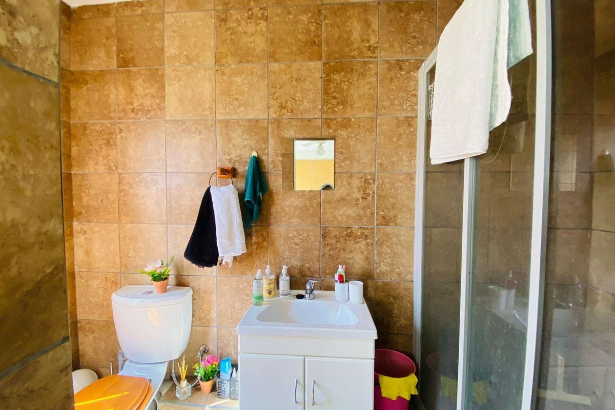 A functional bathroom featuring a vanity basin, a toilet, and a glass-enclosed shower stall with full-height brown wall tiling.