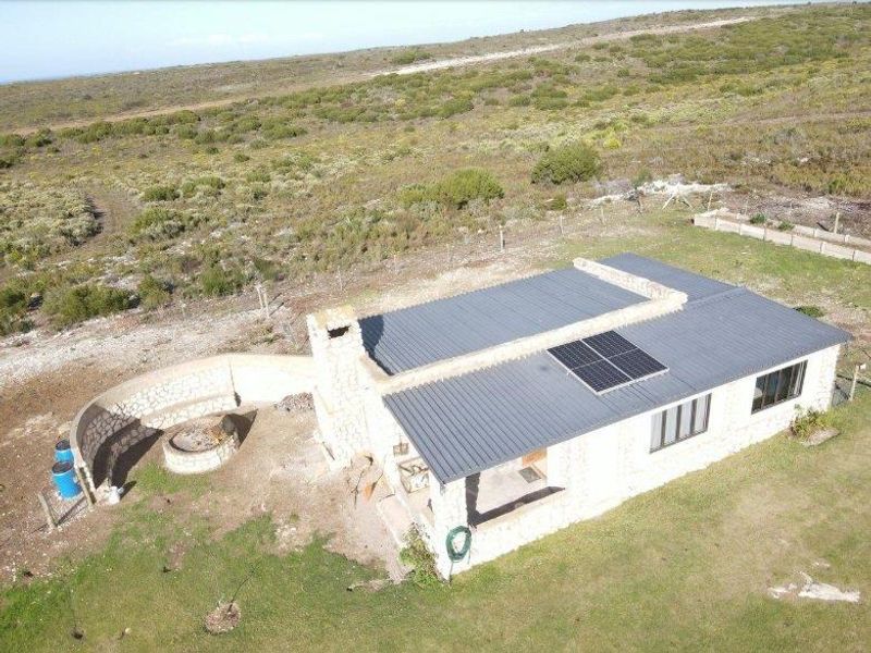 Aerial view of a stone-clad farmhouse featuring a corrugated metal roof, solar panels, and an outdoor stone-walled fire pit area.