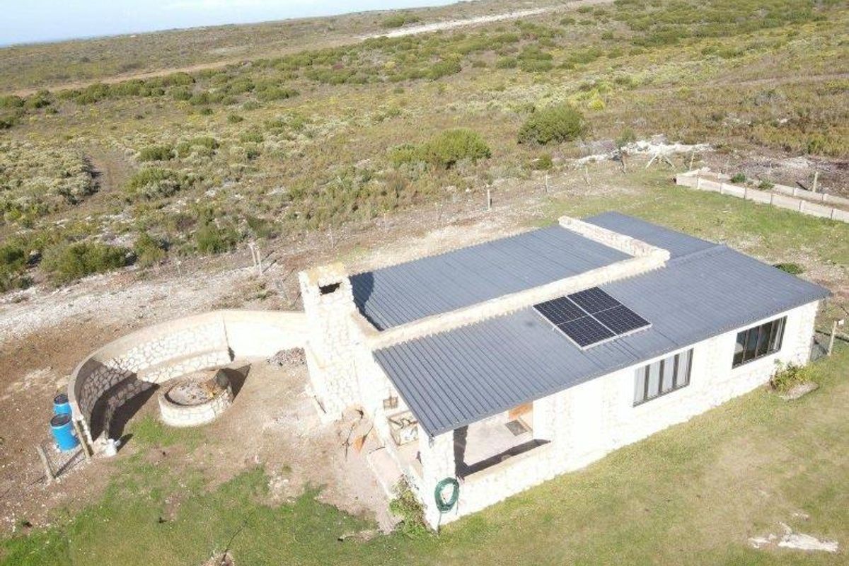 Aerial view of a stone-clad farmhouse featuring a corrugated metal roof, solar panels, and an outdoor stone-walled fire pit area.
