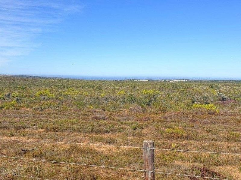 Expansive rural landscape view featuring natural vegetation and open terrain, framed by a simple wire and timber post boundary fence.