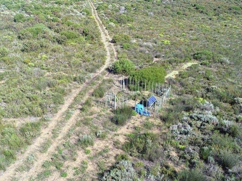 Aerial view of a remote farm plot featuring a small fenced enclosure with solar power infrastructure and a dirt access track.