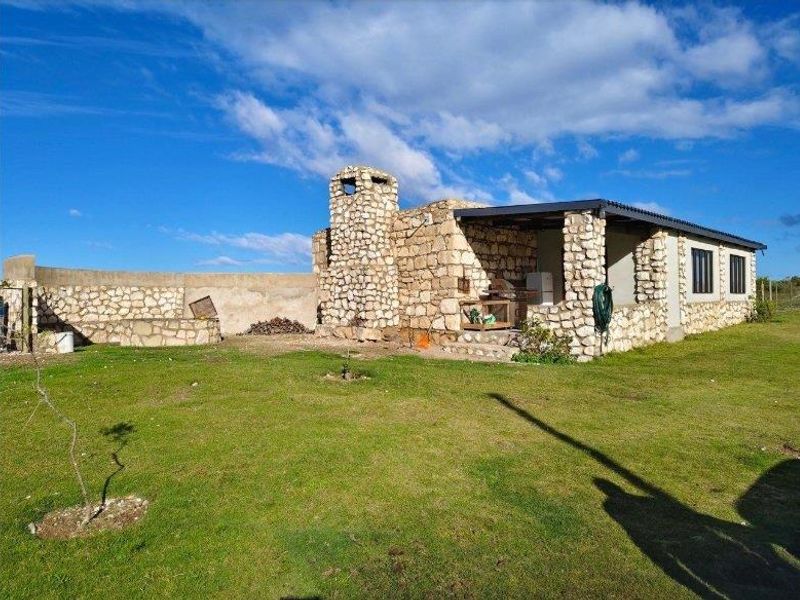 A rustic stone-clad farmhouse exterior featuring a covered patio area, integrated stone chimney, and expansive surrounding lawn.