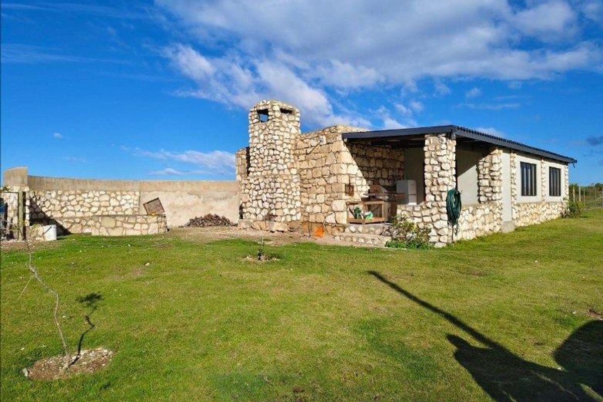 A rustic stone-clad farmhouse exterior featuring a covered patio area, integrated stone chimney, and expansive surrounding lawn.