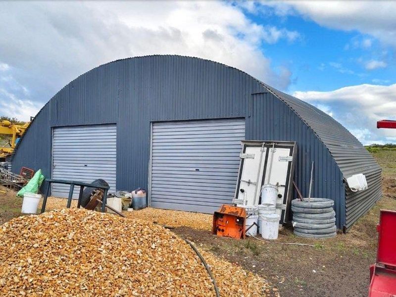 A large, arched corrugated metal farm shed featuring dual roller shutter doors, suitable for storage or agricultural utility purposes.