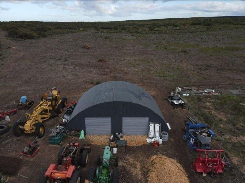 Aerial view of a large arched metal farm shed with dual roller doors, situated on a spacious rural property.