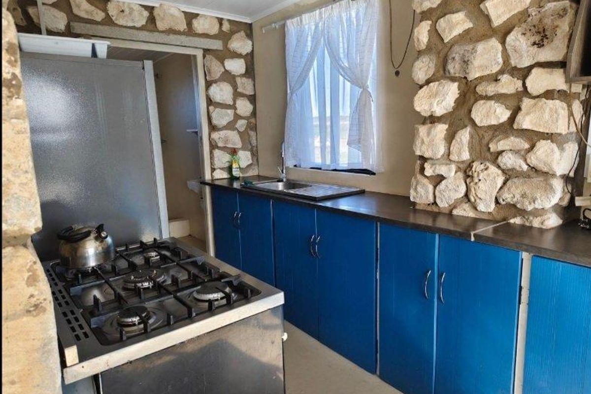 Rustic kitchen featuring exposed stone wall accents, blue cabinetry, and a gas stove, offering a unique farmhouse aesthetic.