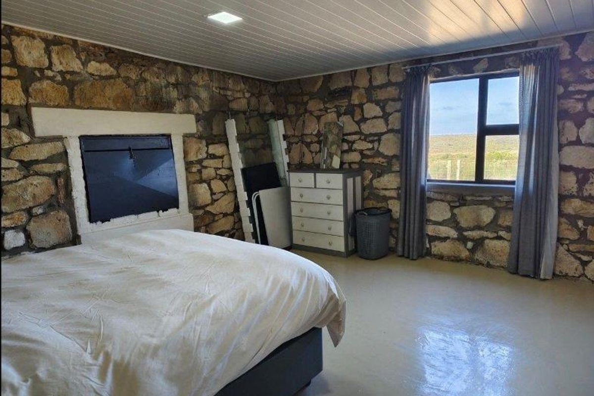 Rustic bedroom featuring exposed natural stone walls, a painted timber ceiling, and a window offering expansive rural views.
