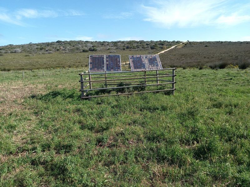 A small solar panel array mounted within a protective metal enclosure, situated in an open field on the farm property.