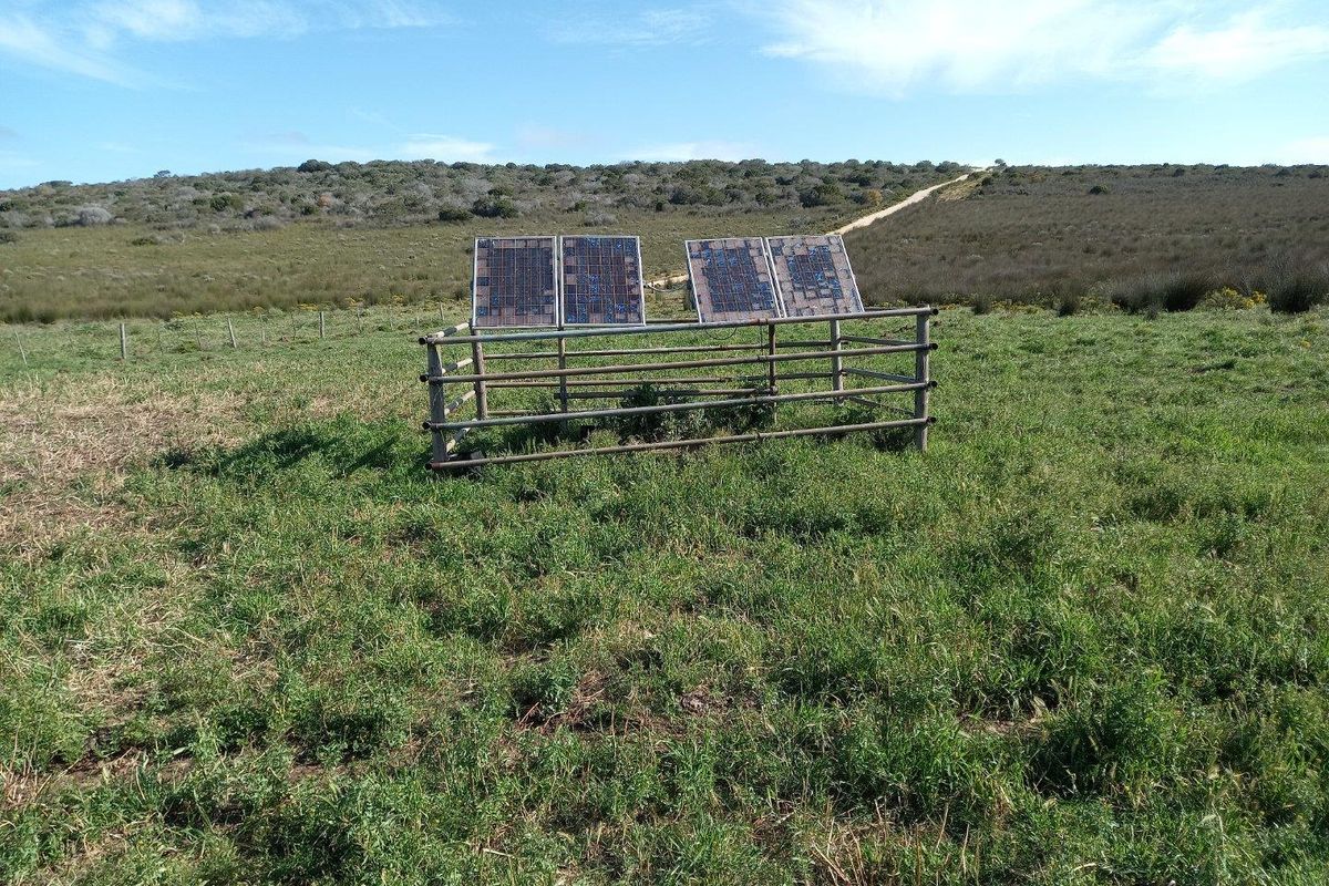 A small solar panel array mounted within a protective metal enclosure, situated in an open field on the farm property.