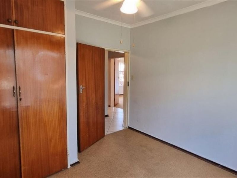 An empty bedroom featuring built-in wooden cupboards, a ceiling fan, and carpeted flooring, offering a blank canvas for personalization.