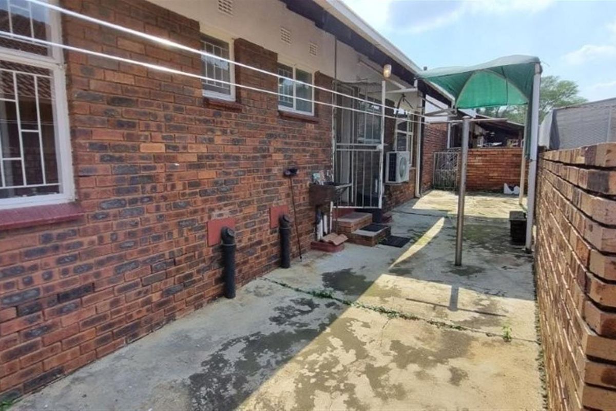 Rear exterior view of the townhouse featuring a brick facade, concrete paved courtyard area, and perimeter brick boundary wall.