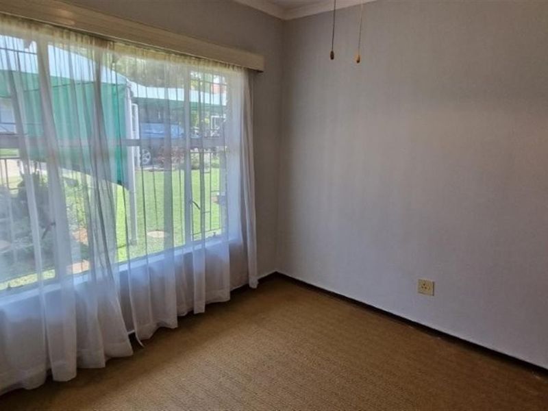 A vacant bedroom featuring carpeted flooring, a built-in cupboard, and a large window fitted with security bars.