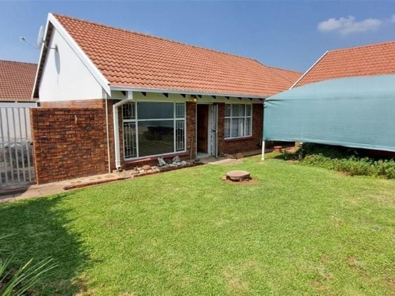 Front view of a brick townhouse featuring a tiled roof, lawn area, and secure gated access.