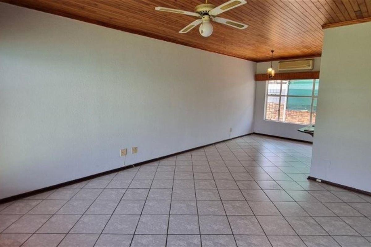 Spacious, empty living area featuring tiled flooring, a timber-clad ceiling with a fan, and a wall-mounted air conditioning unit.