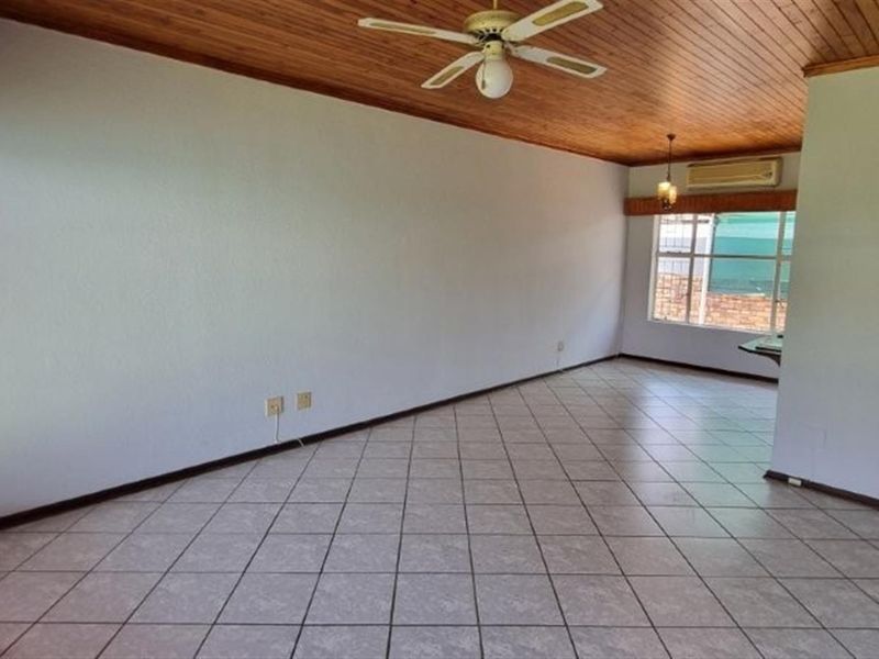 Spacious, empty living area featuring tiled flooring, a timber-clad ceiling with a fan, and a wall-mounted air conditioning unit.