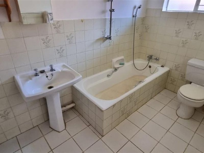 A dated bathroom featuring a pedestal basin, built-in bathtub with shower mixer, and a standard toilet, finished with original ceramic wall and floor tiles.