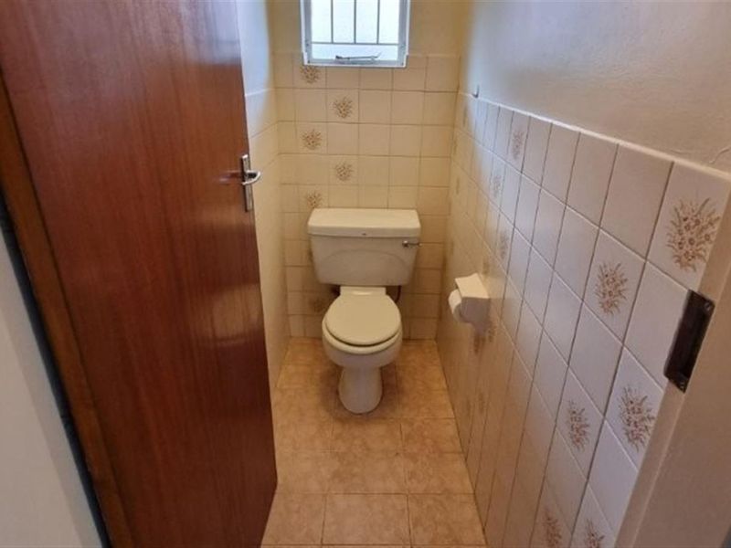 A compact, dated guest toilet featuring ceramic wall and floor tiles, providing a functional space ready for modernization.