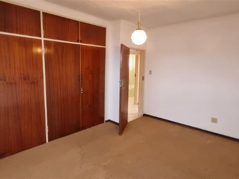 A spacious, empty bedroom featuring extensive built-in wooden cupboards and carpeted flooring, offering a blank canvas for renovation or modern interior design updates.
