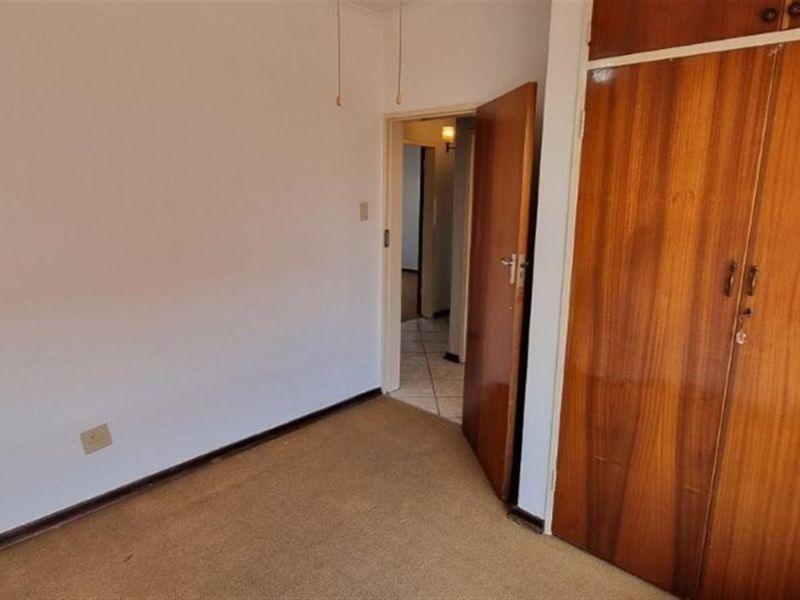 An empty bedroom featuring built-in wooden cupboards and carpeted flooring, offering a blank canvas for renovation or restyling.