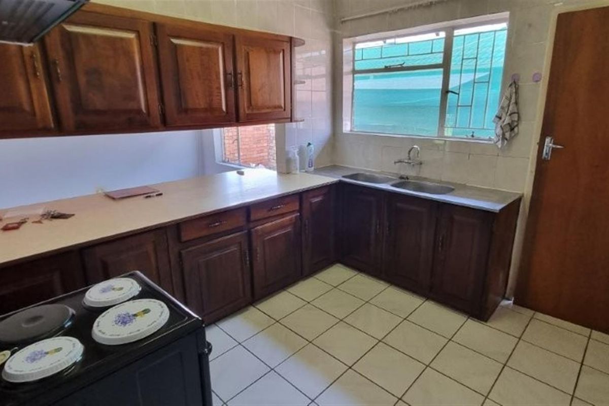 A functional kitchen featuring wooden cabinetry, tiled flooring, a double sink, and a tiled backsplash, offering a classic layout with potential for modernization.