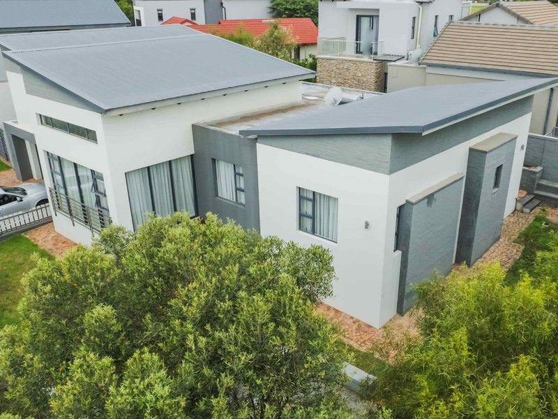 Aerial view of a modern residential property featuring a contemporary skillion roof design, paved driveway, and landscaped garden surroundings.