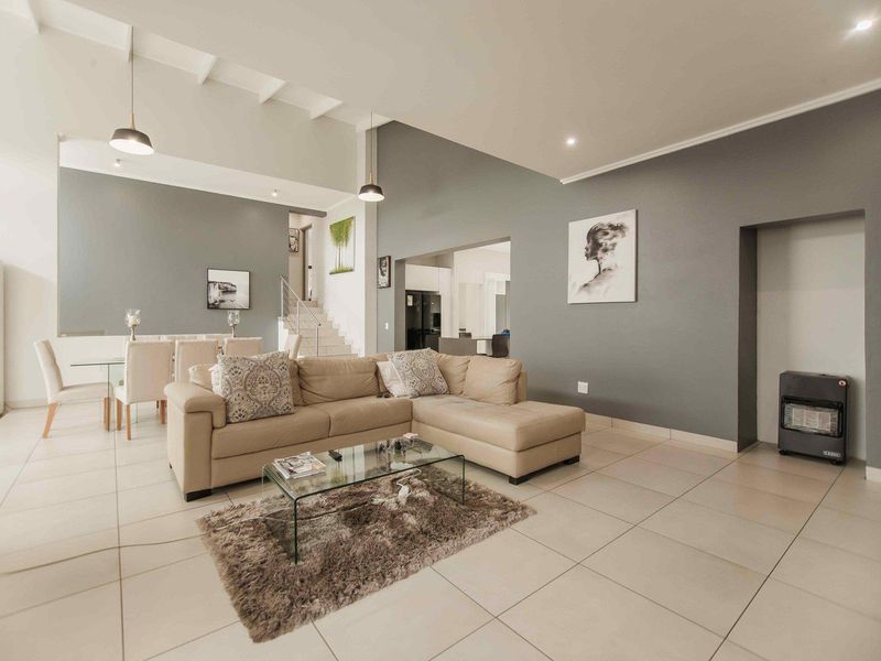 Spacious open-plan living and dining area featuring high vaulted ceilings, neutral tiled flooring, and modern recessed and pendant lighting.