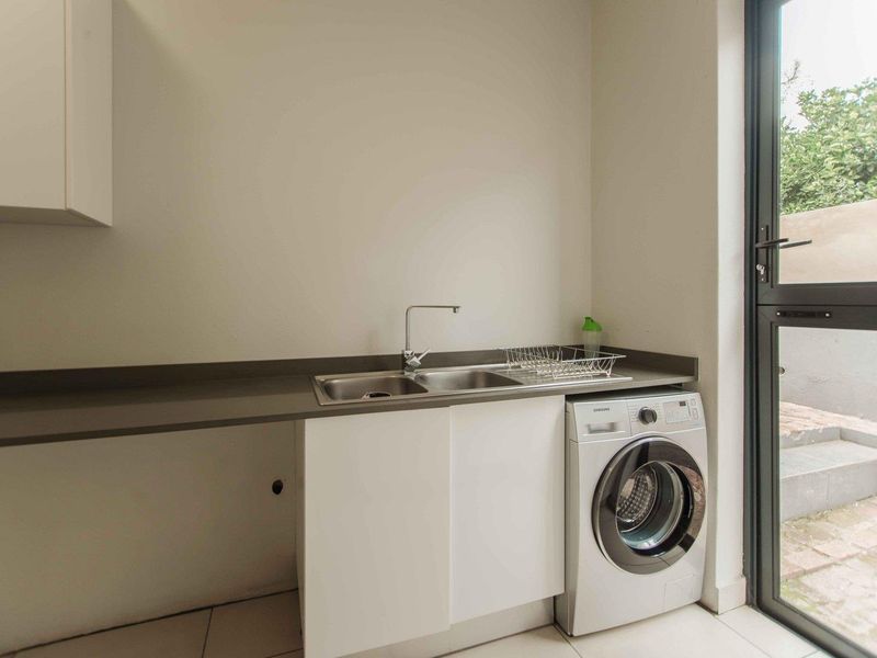 A functional laundry area featuring a stainless steel double sink, laminate countertop, built-in cabinetry, and direct access to the exterior.