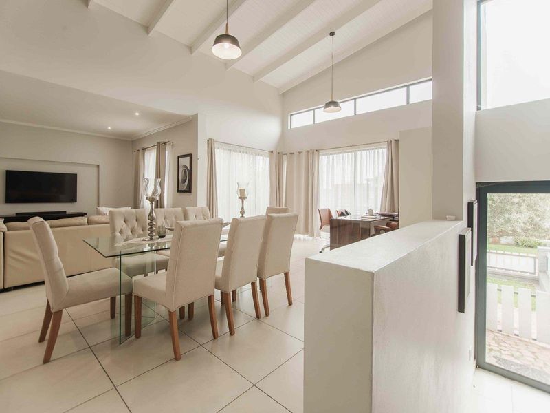 Spacious open-plan living and dining area featuring high vaulted ceilings with exposed beams, large windows, and modern tiled flooring.