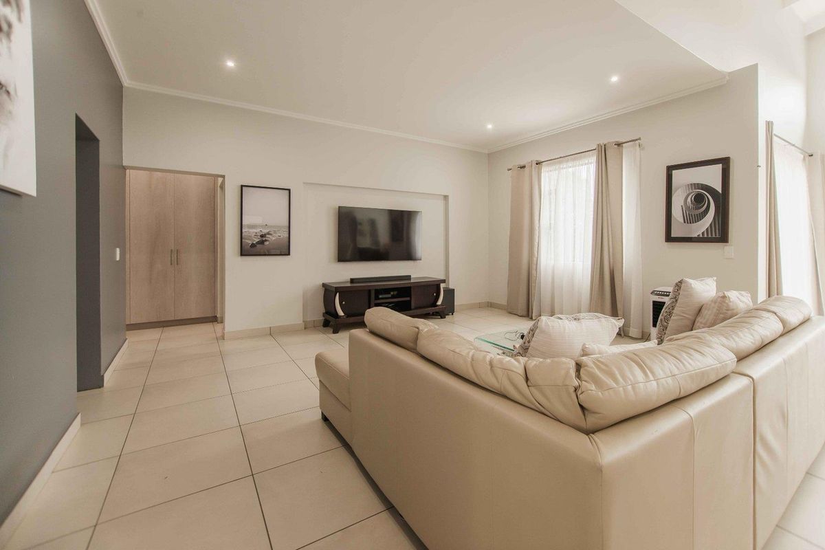 A bright and spacious living room featuring neutral tiled flooring, recessed ceiling lighting, and a convenient built-in storage cupboard.