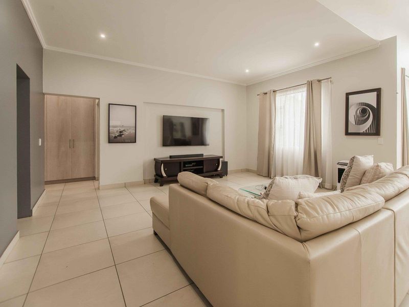 A bright and spacious living room featuring neutral tiled flooring, recessed ceiling lighting, and a convenient built-in storage cupboard.