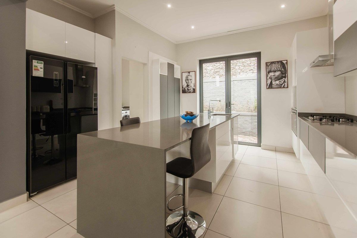 Modern kitchen featuring a central island with stone countertops, gas hob, integrated appliances, and sleek cabinetry, leading out to a private courtyard.
