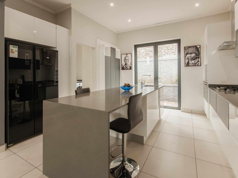 Modern kitchen featuring a central island with stone countertops, gas hob, integrated appliances, and sleek cabinetry, leading out to a private courtyard.