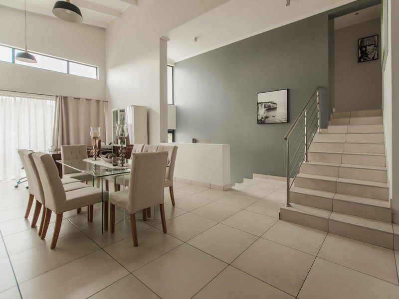 Spacious dining area featuring high vaulted ceilings, large windows for natural light, and a modern staircase with a stainless steel balustrade.