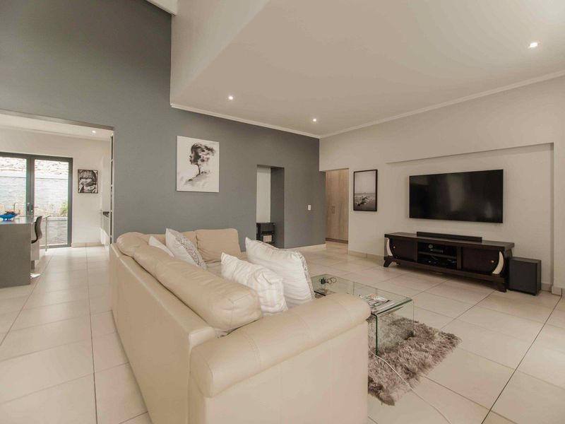 Spacious open-plan living area featuring neutral tiled flooring, recessed lighting, and a modern grey accent wall with seamless flow to the outdoor space.