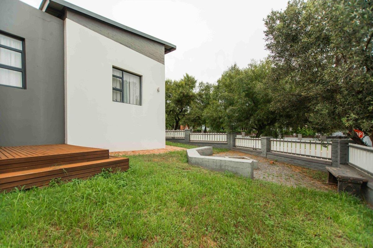 Rear garden area featuring a timber deck, paved section with a low concrete retaining wall, and perimeter fencing.