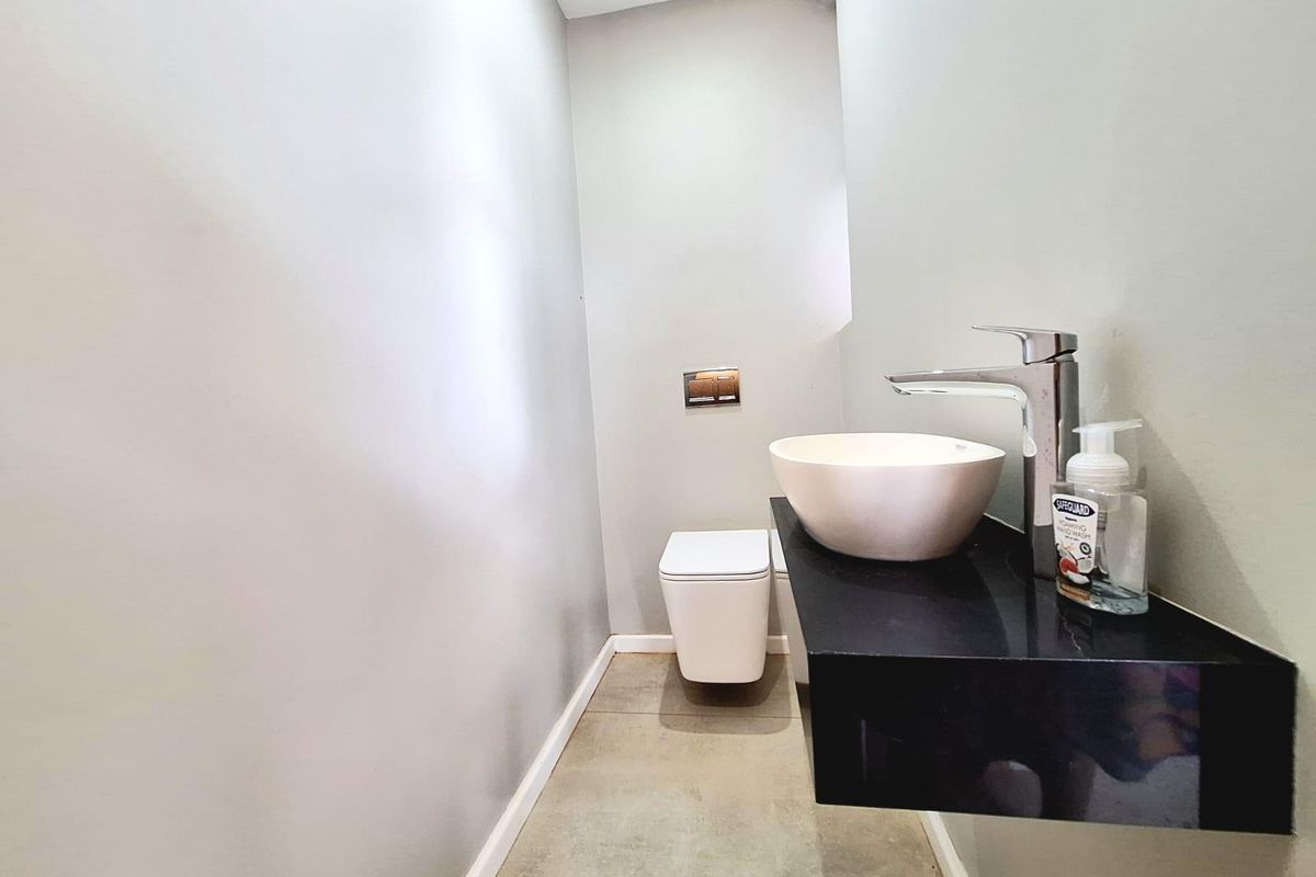 A modern guest bathroom featuring a wall-mounted toilet with a concealed cistern and a contemporary vessel sink set on a floating black vanity shelf.