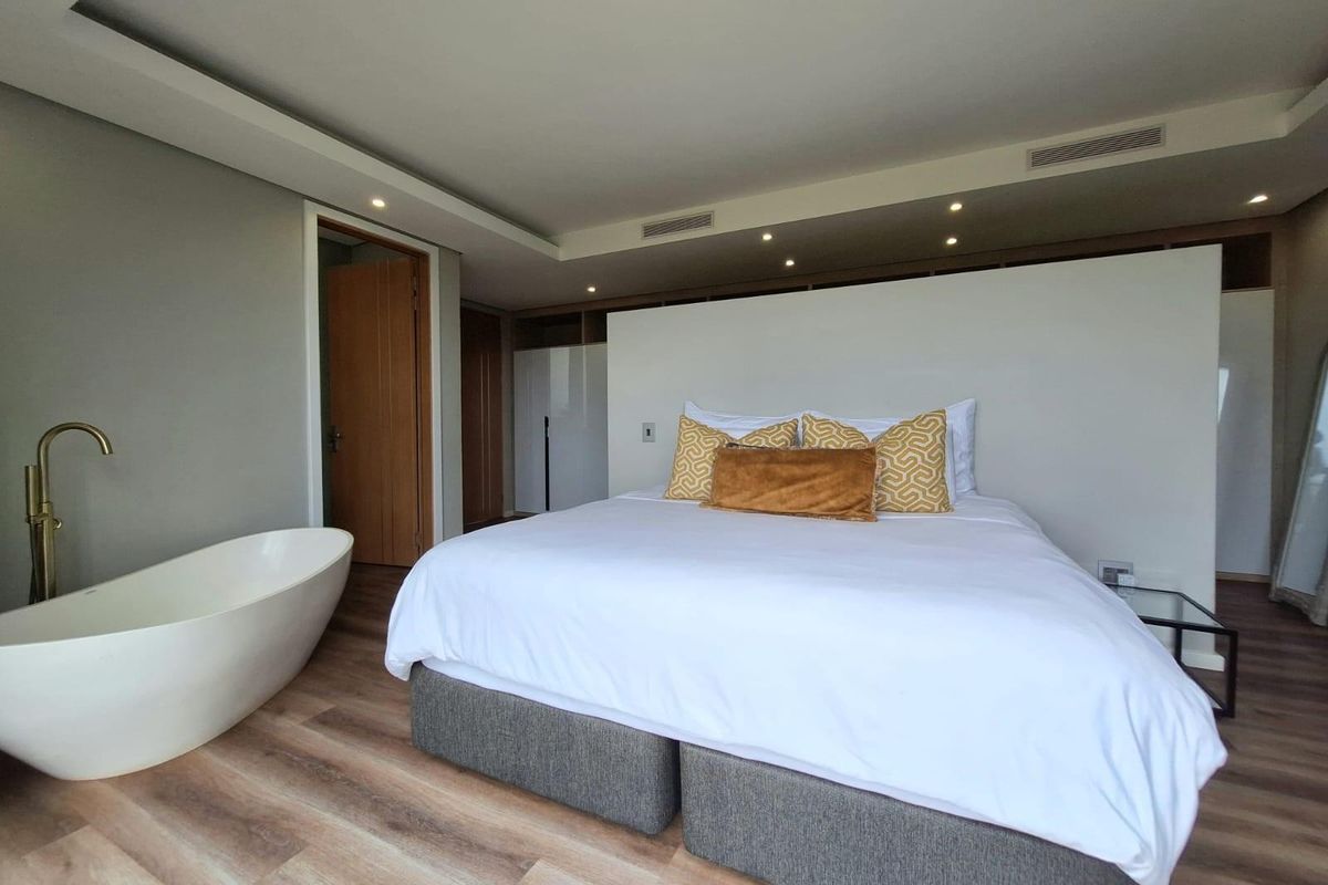 A modern bedroom suite featuring a freestanding bathtub with brass fixtures, recessed ceiling lighting, and integrated storage cabinetry.