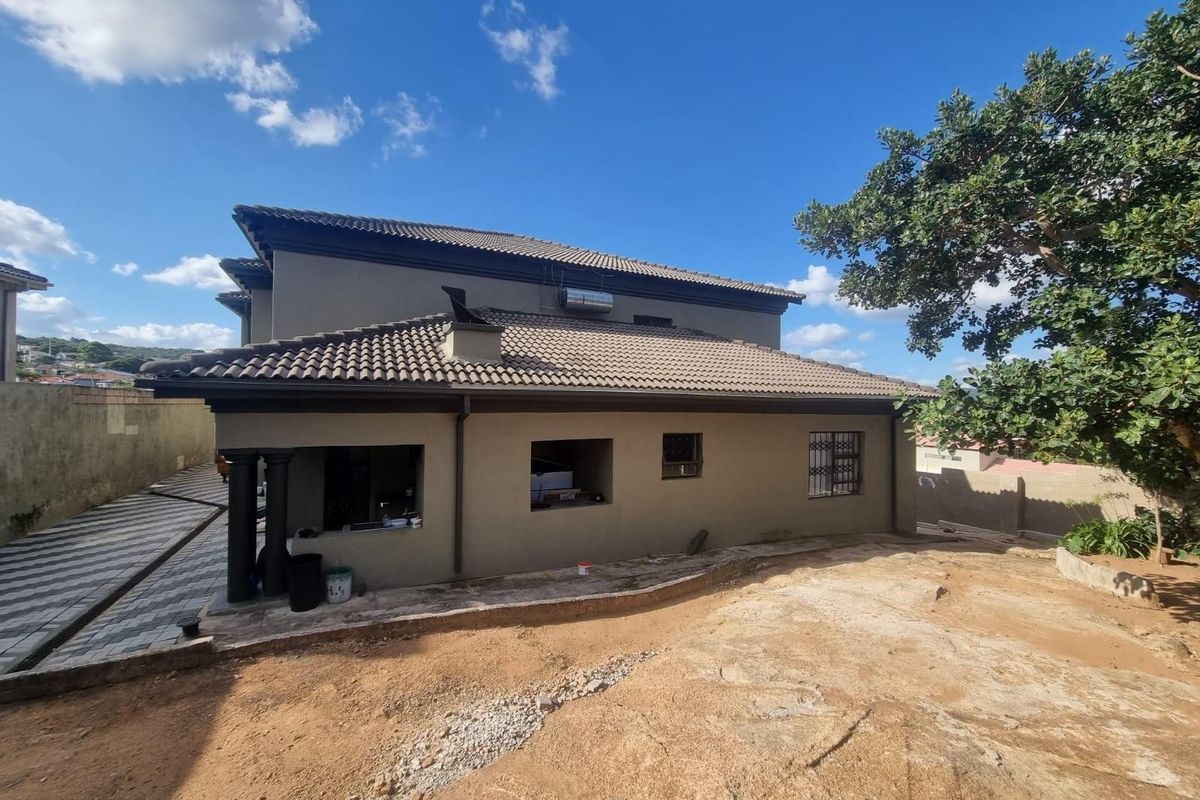 Rear view of the two-story house featuring a tiled roof, neutral exterior walls, and an unfinished garden area with paved driveway access.