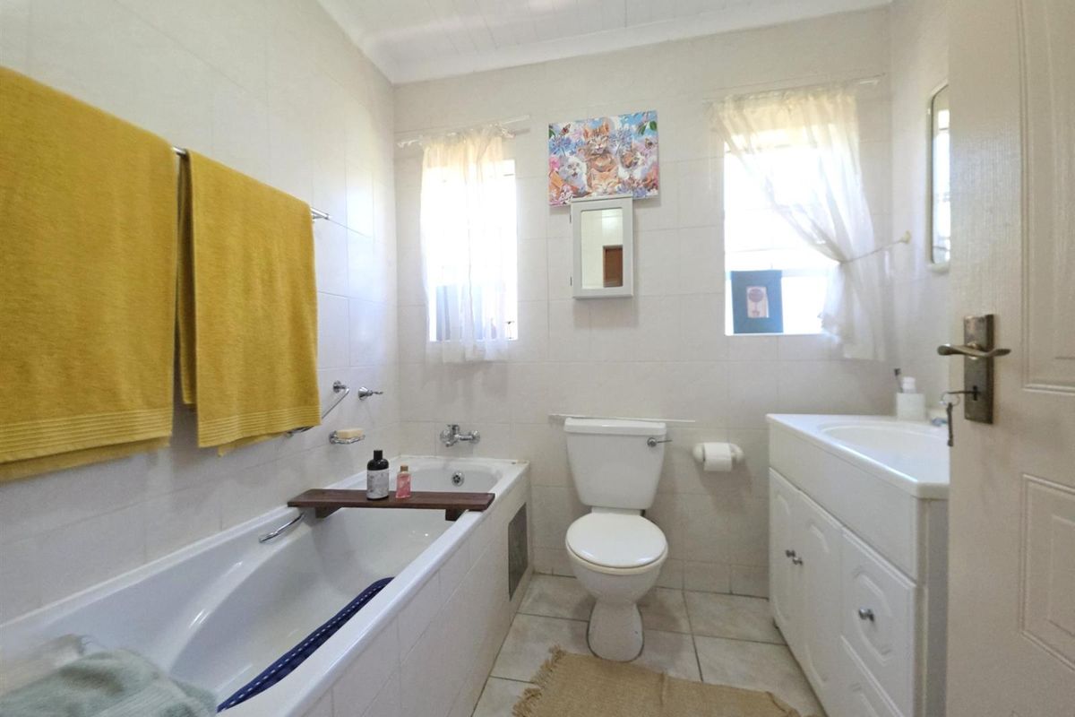 A functional bathroom featuring a built-in bathtub, a standard toilet, and a vanity cabinet with an integrated washbasin, finished with neutral wall tiles.