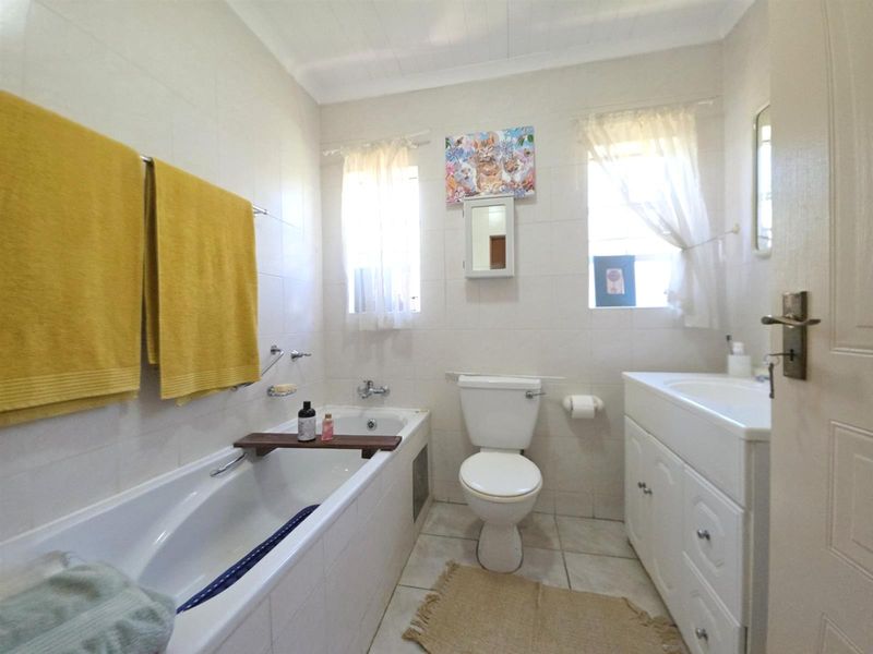 A functional bathroom featuring a built-in bathtub, a standard toilet, and a vanity cabinet with an integrated washbasin, finished with neutral wall tiles.