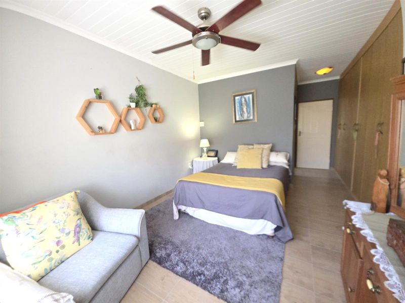 A spacious bedroom featuring built-in cupboards, tiled flooring, and a ceiling fan, offering a comfortable and functional living space.