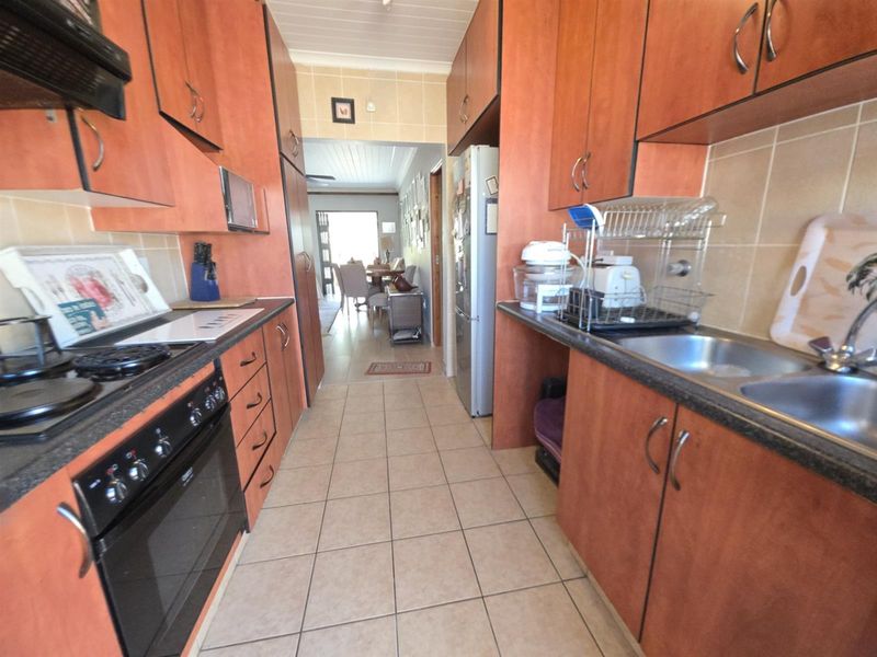 A functional galley-style kitchen featuring laminate cabinetry, tiled flooring, and built-in cooking appliances, leading through to an open-plan dining area.